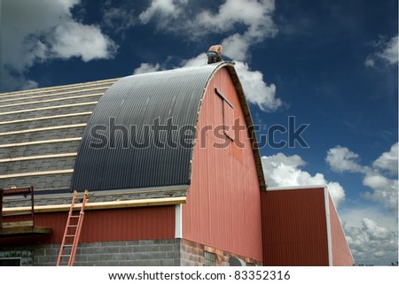 construction worker roofing a red barn