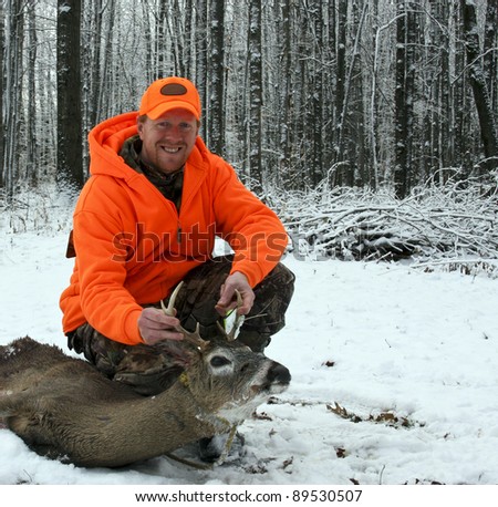 hunter in safety orange with a whitetail deer harvested against a snow and tree background
