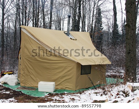 wilderness campsite with a canvas tent on snow covered ground with trees in the background
