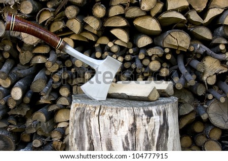 hatchet stuck in a stump with chopped wood and logs  in the background