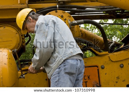 worker repairing a hydraulic hose on machinery equipment wearing a yellow hard hat