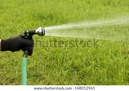 spray of water coming from a garden hose while watering a green grass lawn