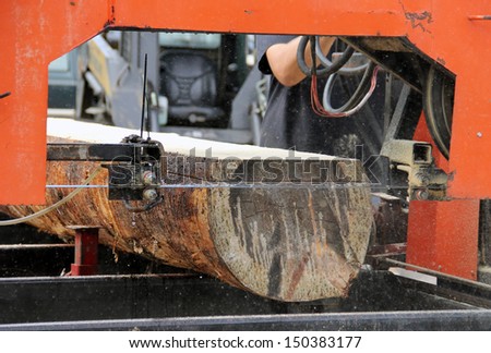 portable saw mill cutting a log into lumber with saw dust in the air from the cutting