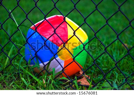 Closeup of discarded beach ball behind chain link fence.