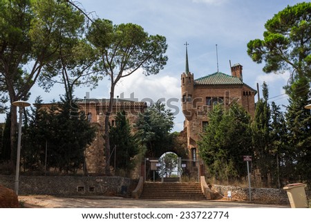 The School and the Teacher\'s House of the Colonia Guell. On the left stands the school, with a Stone facade and large Windows. On the right can be seen the turret.