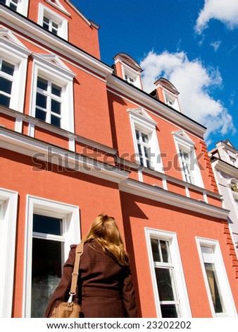 Woman standing in front of house and looking to buy a flat