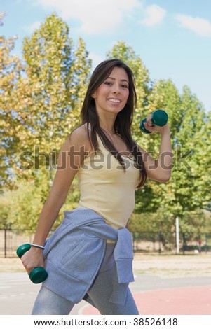 Young attractive girl with weights in her hands exercise outdoors