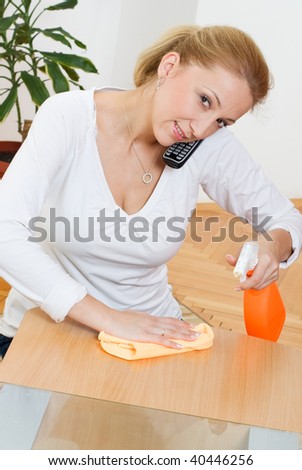 stock photo Young blonde housewife cleaning a table while talking phone