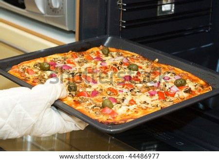 Closeup of gloved  hand taking a roasted pizza out of the oven