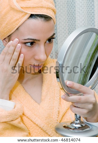 Young woman with yellow towel on head ooking  at her face  in the mirror