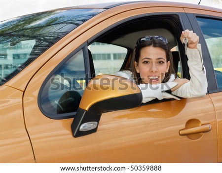 Beautiful young woman sitting in the car and holding a car keys in her hand