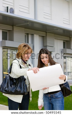 Real Estate woman Agent  standing  with young woman customer in front  of a new building and showing a scheme of flat