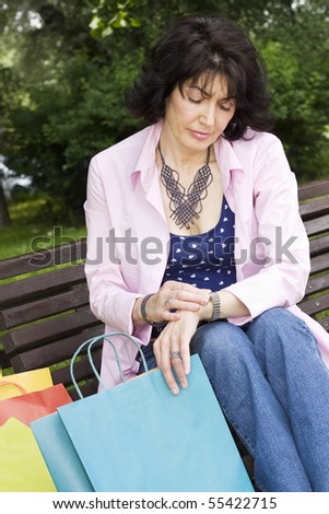 Beautiful mature woman sitting on the park bench and looking at watch.