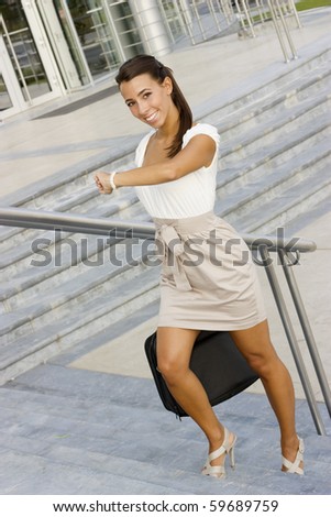 Smiling young businesswoman walking up stairs and checking the  time on her watch in front of office building