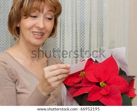 Charming mature woman receiving  a  Poinsettia flowers and reading a greeting card.
