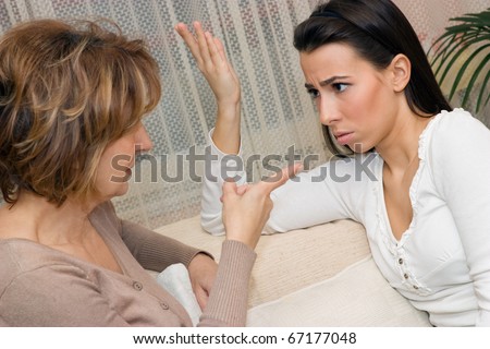 Mature mother and her daughter sitting on the sofa and serious talking.