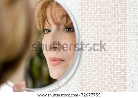 Charming mature woman looking at her face in the mirror.