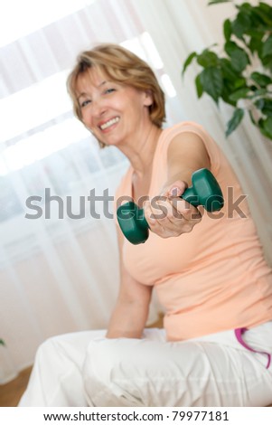 Charming Mature woman  sitting on the floor and exercising with dumbbells at home. Focus on the hand.