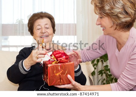 Happiness senior woman getting a red Christmas Present from a mature nurse.