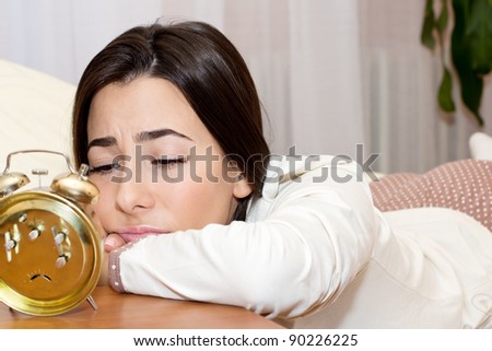 Beautiful young woman lying in the bed and tired looking in the alarm clock.