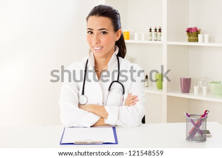 Portrait of serious young doctor sitting at the table and holding a stethoscope in hands.