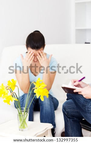 Young woman sitting on the sofa with head in hands and talking with therapist.