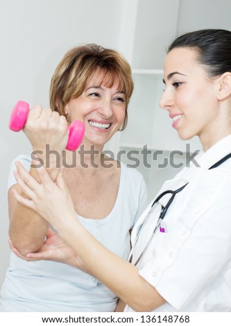 Charming  mature patient lifts dumbbells with a young physical therapist.