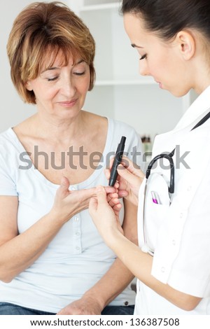 Young Female Doctor Checking Blood Sugar Level To Mature Patient .