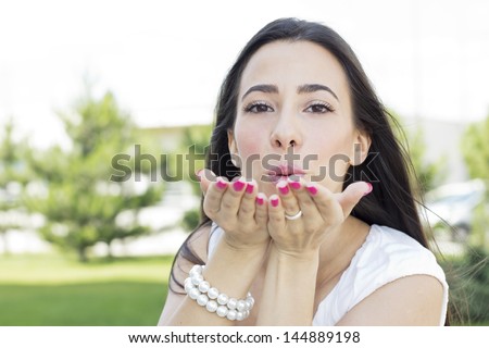 Portrait of cute young female blowing kiss outdoors.