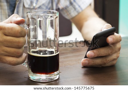 Closeup of male hands with mug of beer and smart phone.