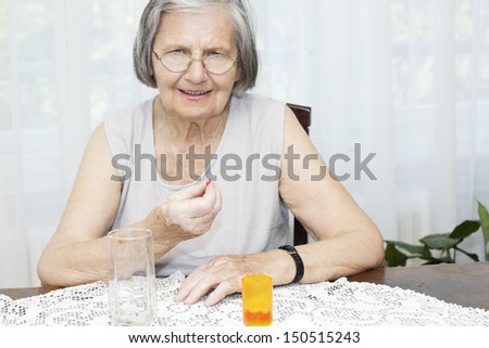 Senior woman sitting at the desk looking at camera and holding a pill.