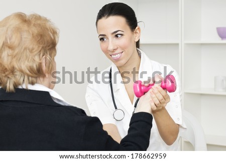Senior female  patient lifts dumbbells with a young nurse at home.