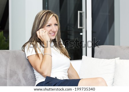 Charming young woman sitting on the sofa and chatting with friends by phone.