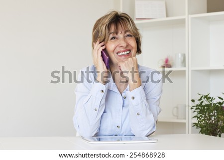 Happiness mature women sitting at the desk with hand on her shin  and talking by smart phone.