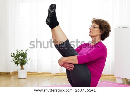 Senior brown haired woman with eyes closed   sitting on the parquet Floor and  exercising yoga at home.