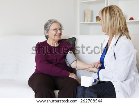 Happiness grandmother sitting on the sofa with her female nurse in the living room . They are  looking at each other while female nurse measuring grandmother a blood pressure.
