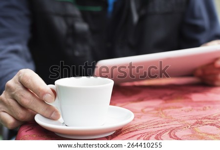 Closeup of male hands with with digital tablet surfing the net .The man sitting at the table in the cafe and drinking a coffee.