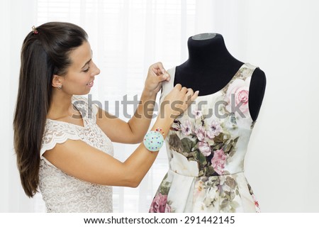 Beautiful young woman making a new dress on the on a tailoring mannequin.