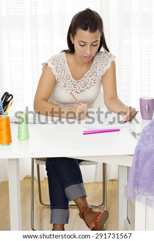 Beautiful  female fashion designer sitting at the desk and  drawing a sketch.