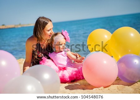 Young mother and beautiful little girl playing with air balloons at the beach