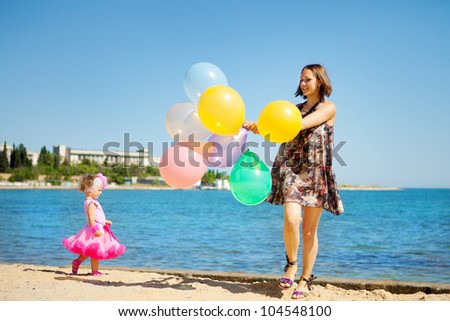 Young mother and beautiful little girl playing with air balloons at the beach