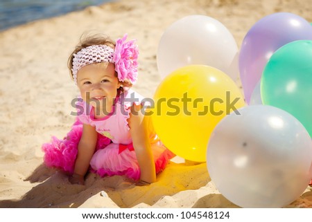 Beautiful little girl playing with air balloons at the beach