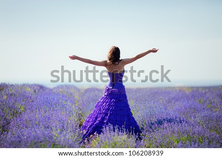 Beautiful woman in a long violet dress standing with open arms on a lavender field