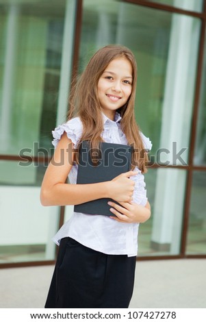 Portrait of a friendly school girl student standing in school uniform and holding book