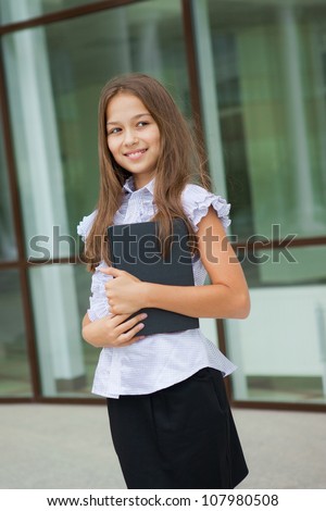 Portrait of a friendly school girl student standing in school uniform and holding book