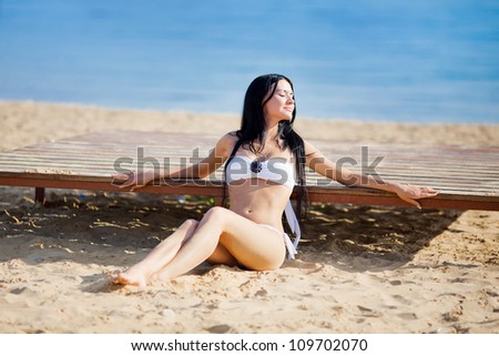 Portrait of beautiful young woman with golden tan resting at beach in summer