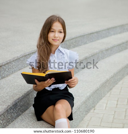 Portrait of a friendly school girl student in school uniform and holding book