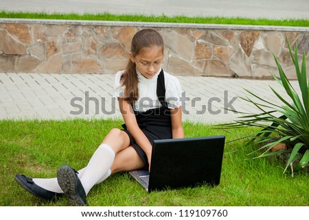 Little student school girl sitting on the grass working on laptop computer at campus