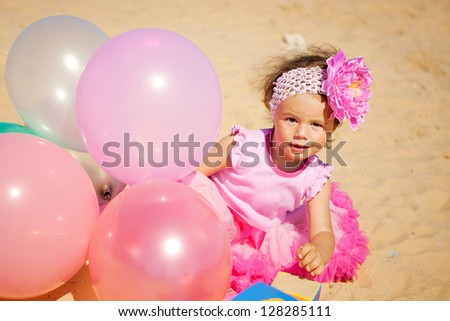 Beautiful little girl playing with air balloons at the beach