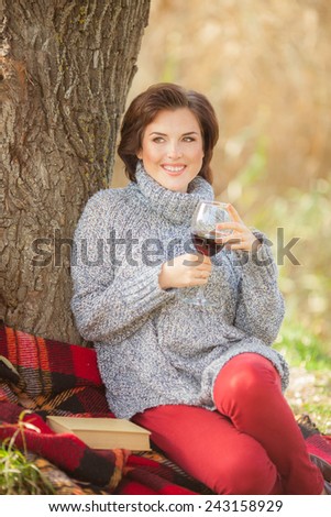 Beautiful woman with wine glass on green background of city park. Romantic girl outdoors. Toned in warm colors.